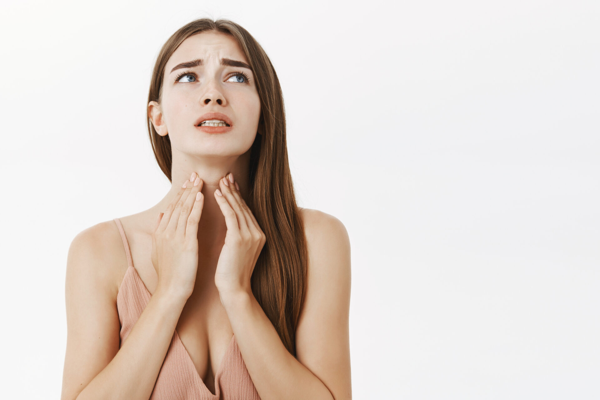 Woman getting ill before important meeting feeling discomfort and suffering from pain in throat touching neck frowning an clenching teeth from terrible feeling posing over gray background